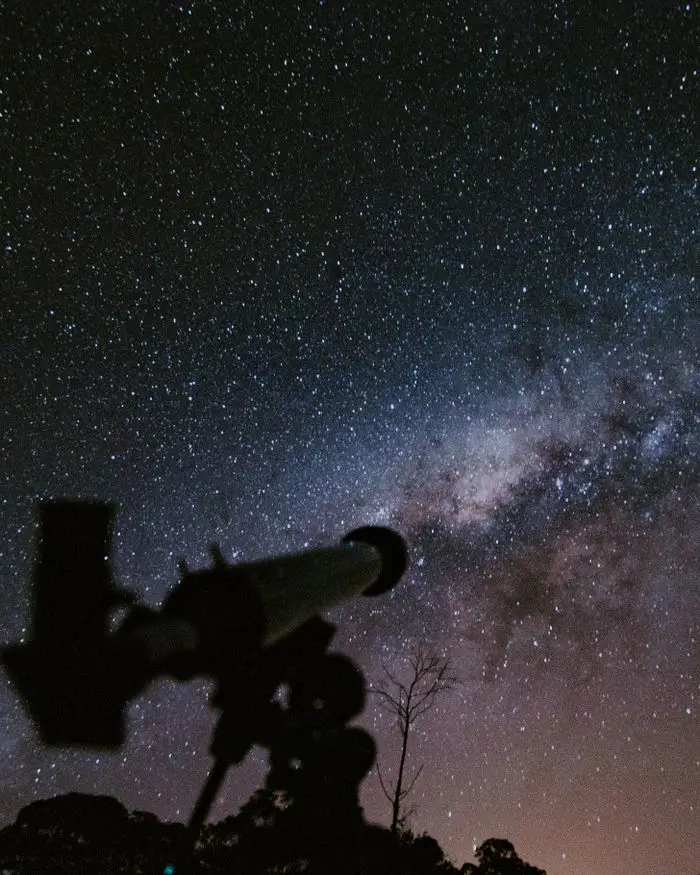 A breathtaking view of the starry night sky with a telescope silhouette capturing the beauty of the cosmos.